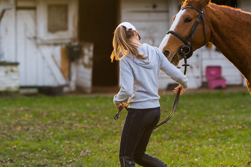 Young pretty girl preparing new horse for ride